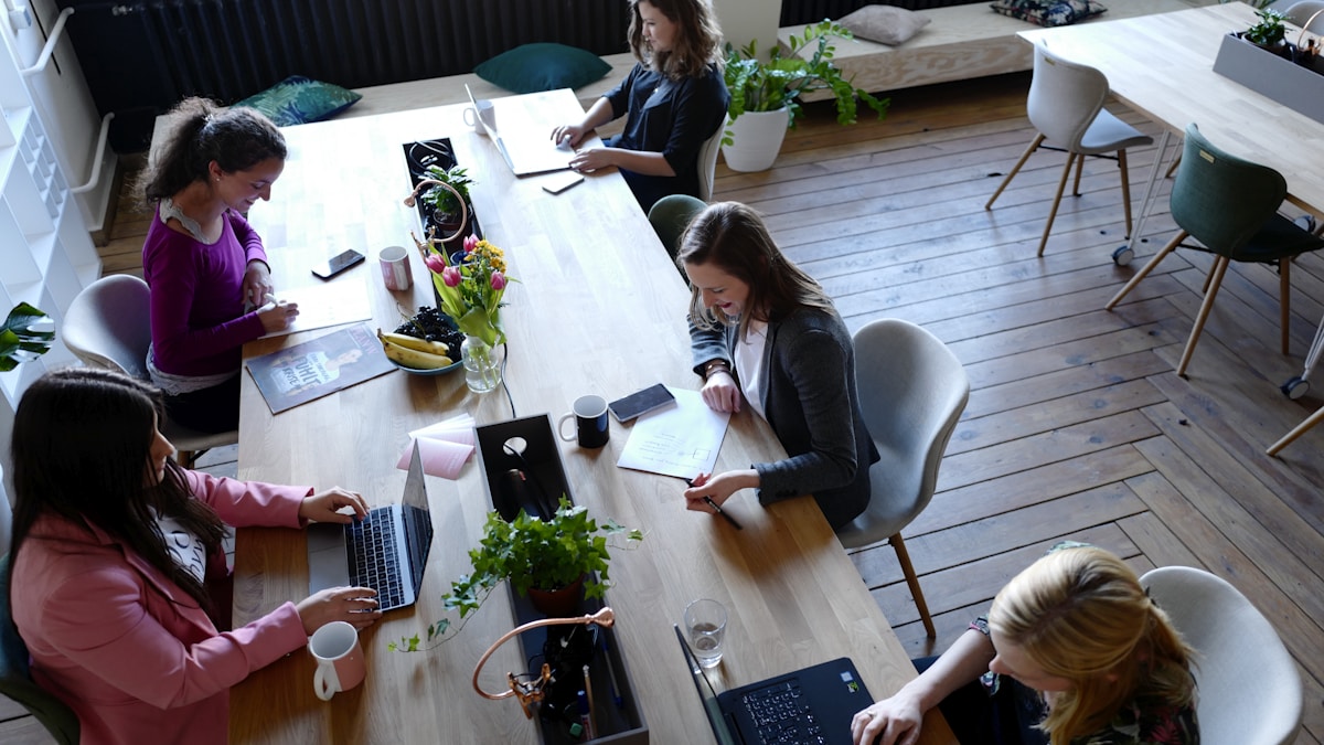 Pessoas em um espaço de coworking moderno, com laptops e interagindo, representando a dinâmica do trabalho global e a troca de informações